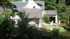 A rustic house with a stone chimney, a small attached structure, and a pond in the foreground. - Le Moulin Bertrand (Benais)