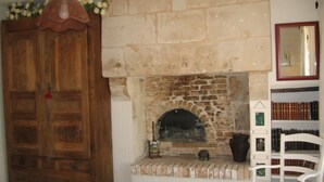 A room with a stone fireplace, a wooden wardrobe, a white chair, and a bookshelf with books. - Le Moulin Bertrand (Benais)