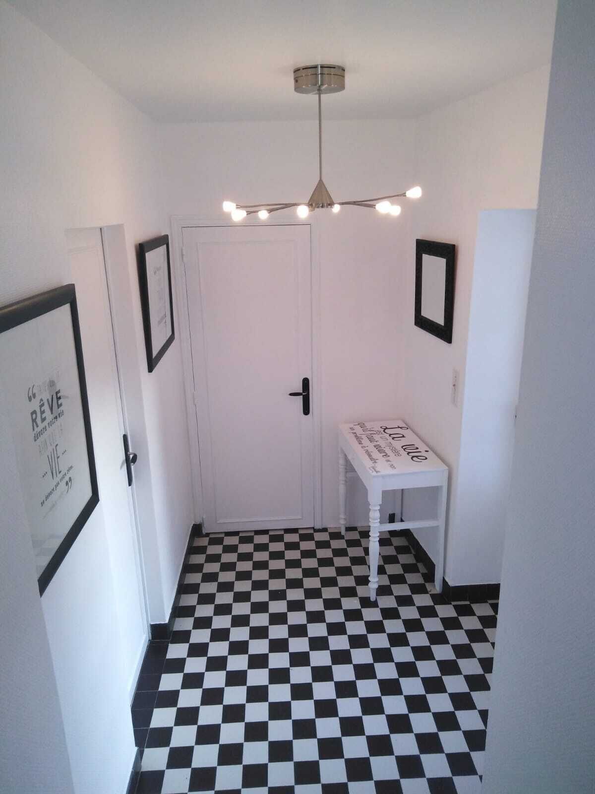 Un couloir doté d’un sol à carreaux, d’une porte blanche et d’une petite table sur laquelle est posé un panneau.