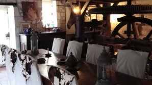 A rustic dining area with a wooden table, white chairs with patterned covers, and a horse head decoration. - Le Moulin Bertrand (Benais)