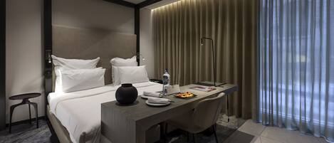 Una habitación de hotel moderna con una cama, un escritorio, una silla, un jarrón, una botella y un plato de comida.