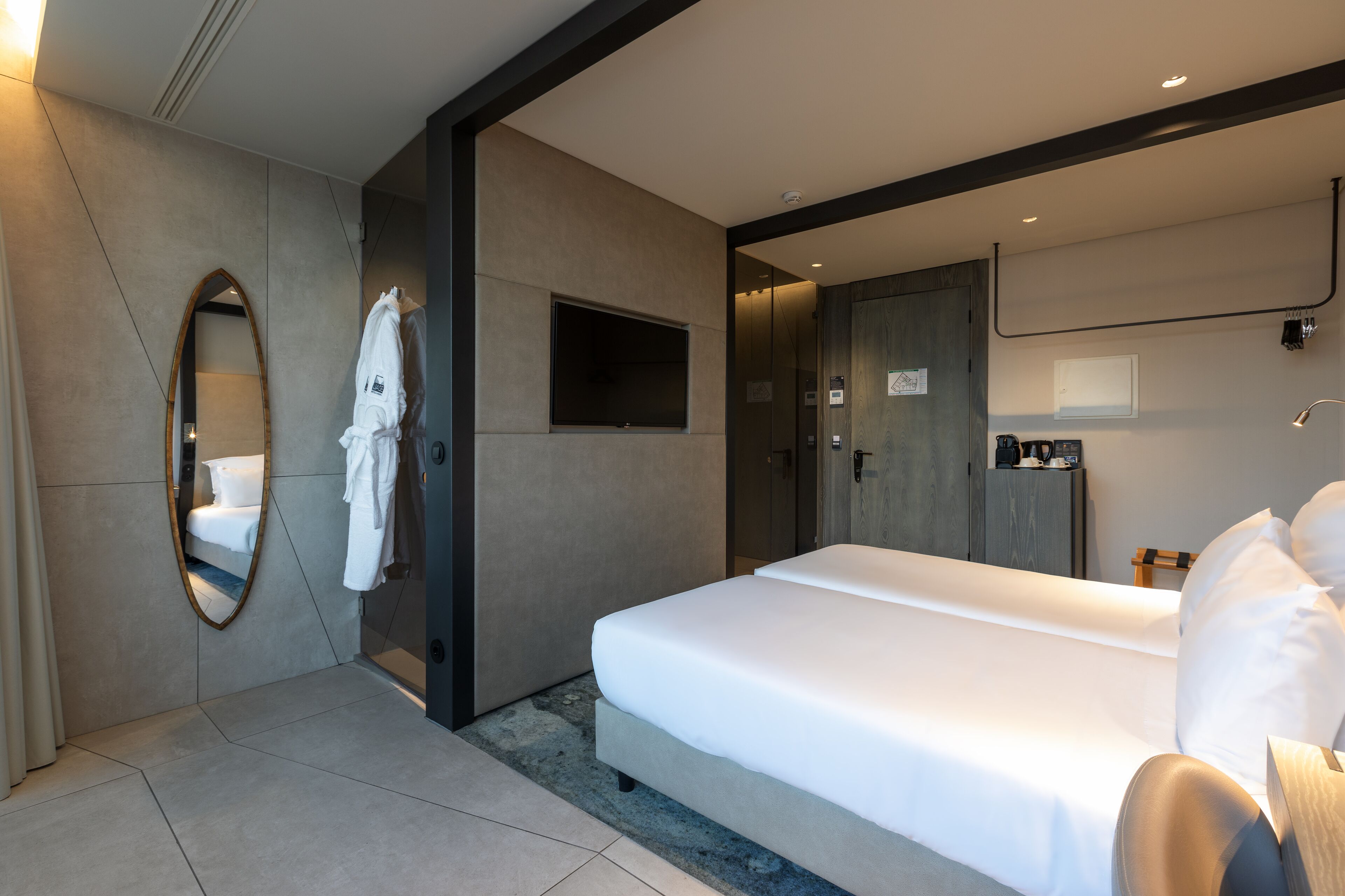 A modern hotel room with a large bed, a mirror, and a robe hanging on the wall.