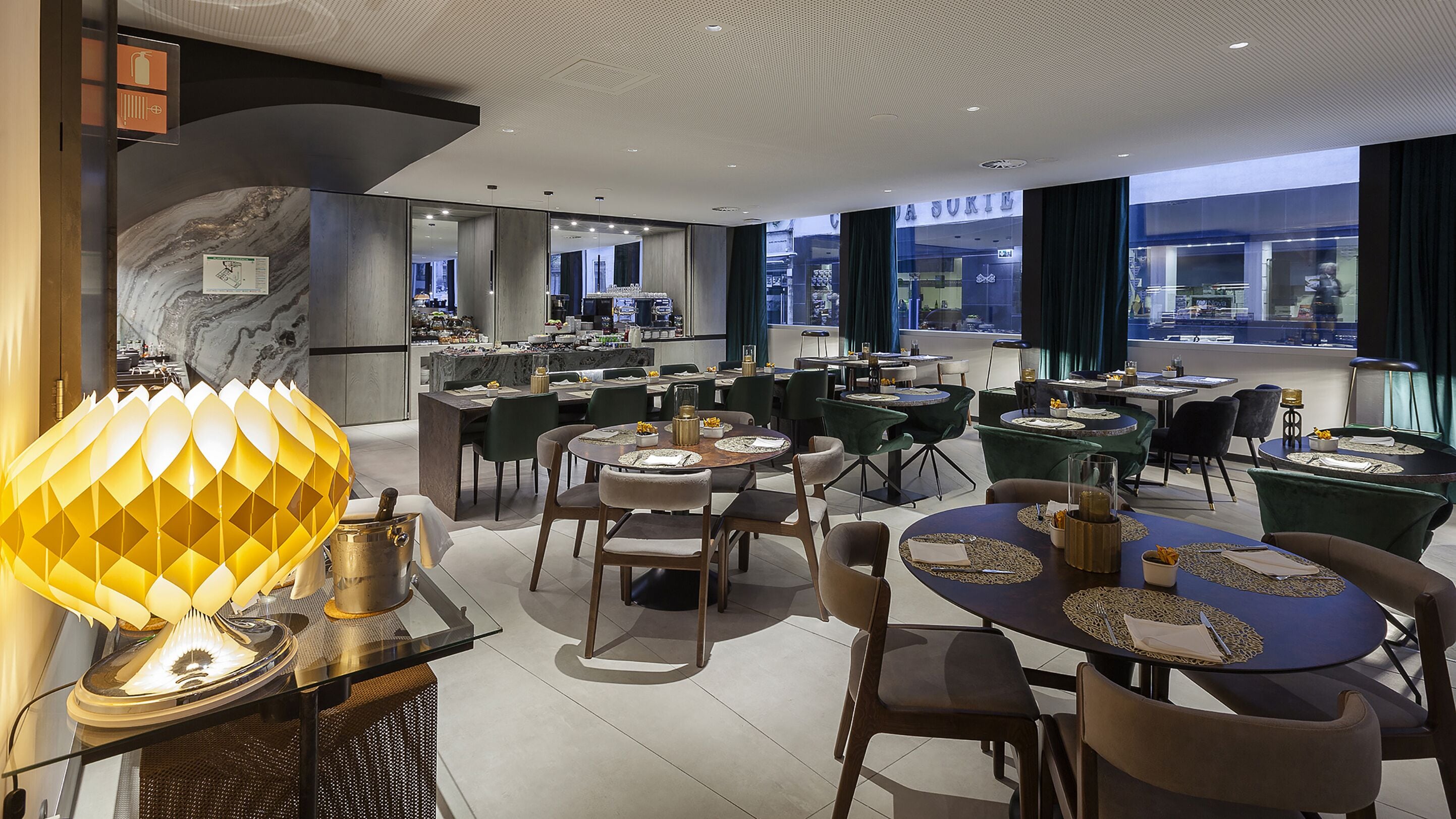 A modern restaurant with round tables, green upholstered chairs, and a decorative lamp.