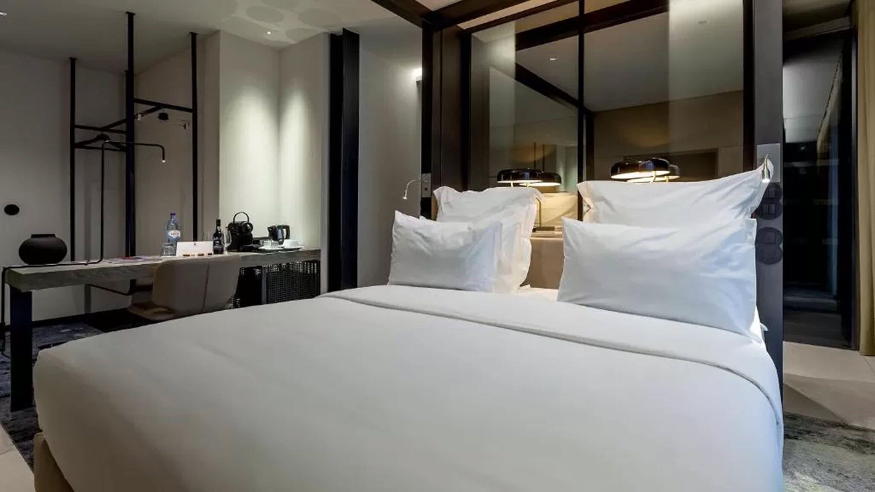 A modern hotel room with a large bed, a desk, and a mirror.