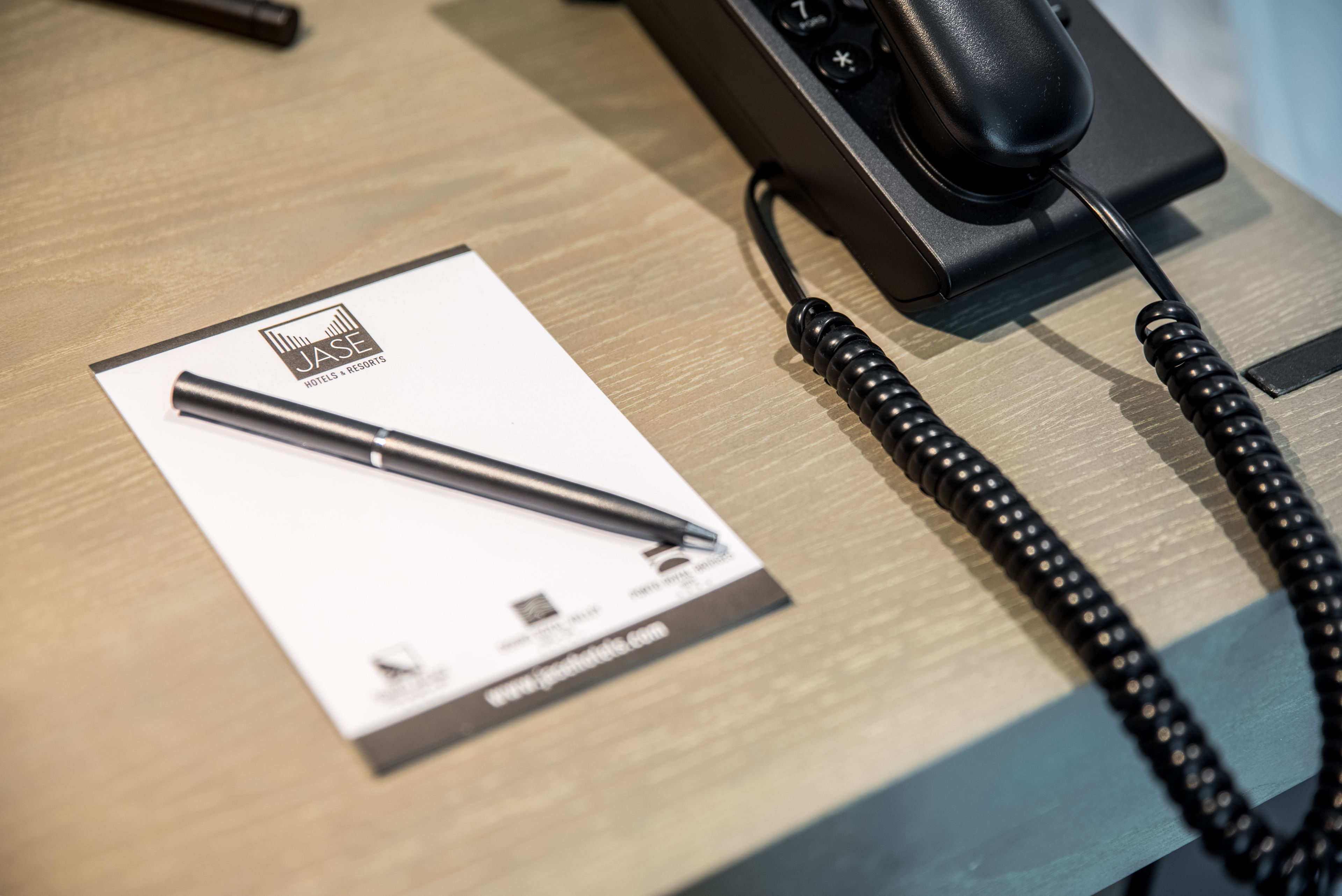 Un escritorio con una pluma, un teléfono y un folleto de JASE Hotels & Resorts.