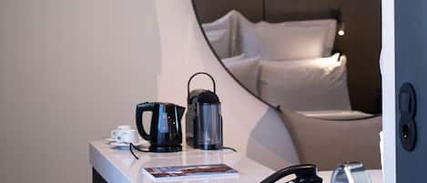 Una habitación de hotel moderna con un espejo redondo, una cama con ropa blanca, una estación de café con hervidor y tazas, un teléfono y un lavabo.