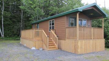 A small wooden cabin with a deck and a staircase leading to a window.