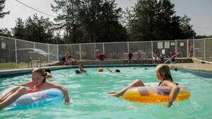 Une piscine avec des bouées gonflables, entourée d’une clôture et d’arbres.