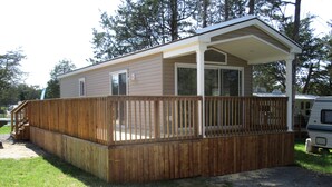 Une maison mobile de plain-pied dotée d’une terrasse en bois et d’un porche couvert.