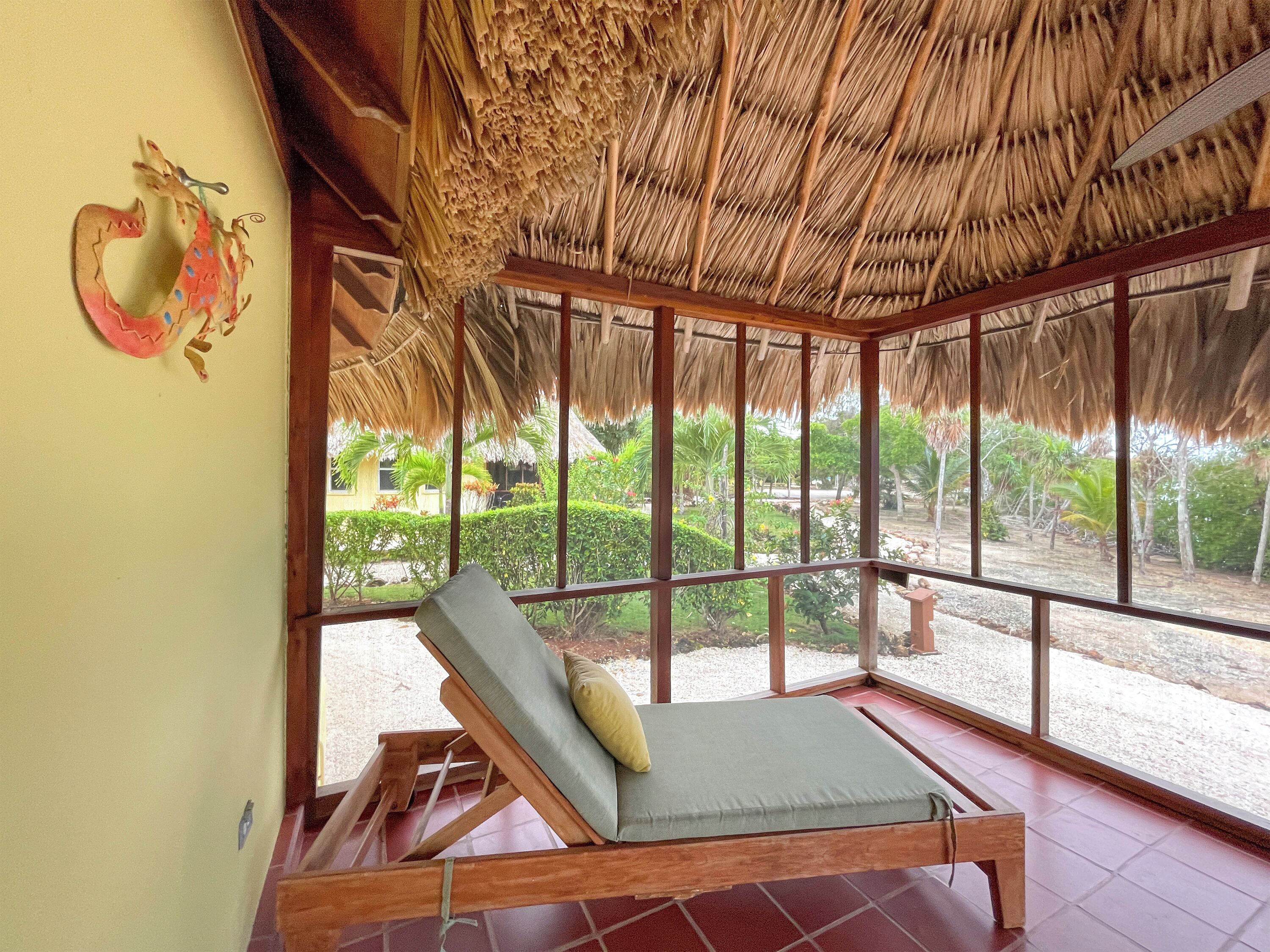 Una habitación con techo de paja, una cama de madera y amplios ventanales con vistas a un jardín.