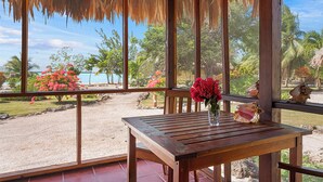 A wooden table with a vase of flowers and a seashell on a patio with a view of a beach and palm trees. - Orchid Bay Resort (Chunox)