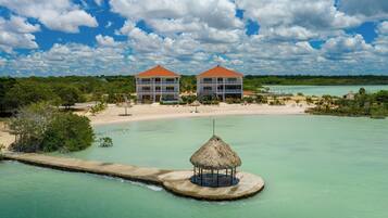 A resort with two large buildings, a beach, and a thatched-roof structure in the water.