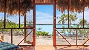 A beachside room with a large window overlooking the sea, a wooden bench, and a thatched roof. - Orchid Bay Resort (Chunox)