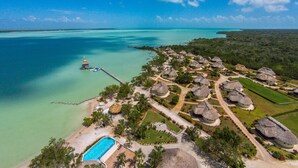 An aerial view of a resort with thatched-roof buildings, a swimming pool, and a pier extending into turquoise waters. - Orchid Bay Resort (Chunox)