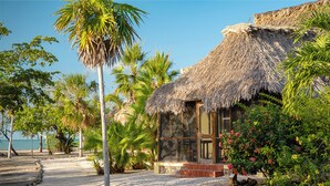 A thatched-roof building with a wooden door and windows, surrounded by palm trees and a gravel path. - Orchid Bay Resort (Chunox)