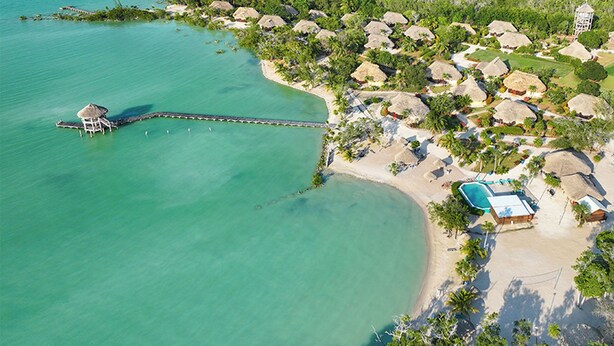 An aerial view of a resort with thatched-roof huts, a swimming pool, and a pier extending into turquoise waters. - Orchid Bay Resort (Chunox)