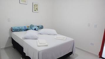 Ein Einzelbett mit weißer Bettwäsche, einem blau-grün gemusterten Kopfkissen und zwei weißen Kissen. Darüber an der Wand hängen zwei gerahmte Kunstwerke.