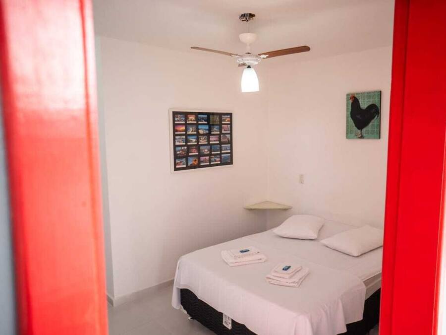 Un dormitorio con cama, ventilador de techo, una composición de fotos en la pared y una pared de acento roja.