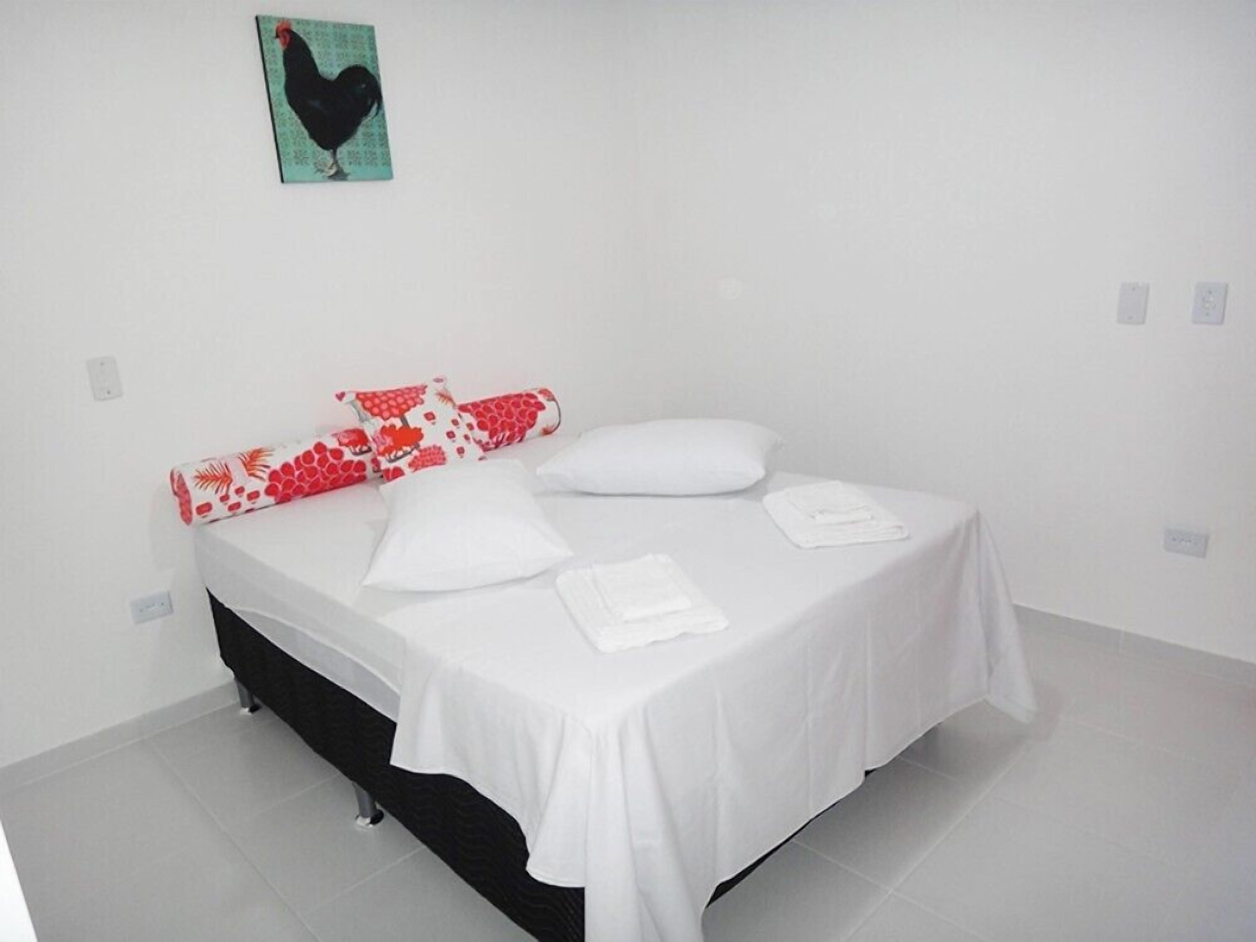 A bed with white bedding, a red and white pillow, and a black and white pillow.