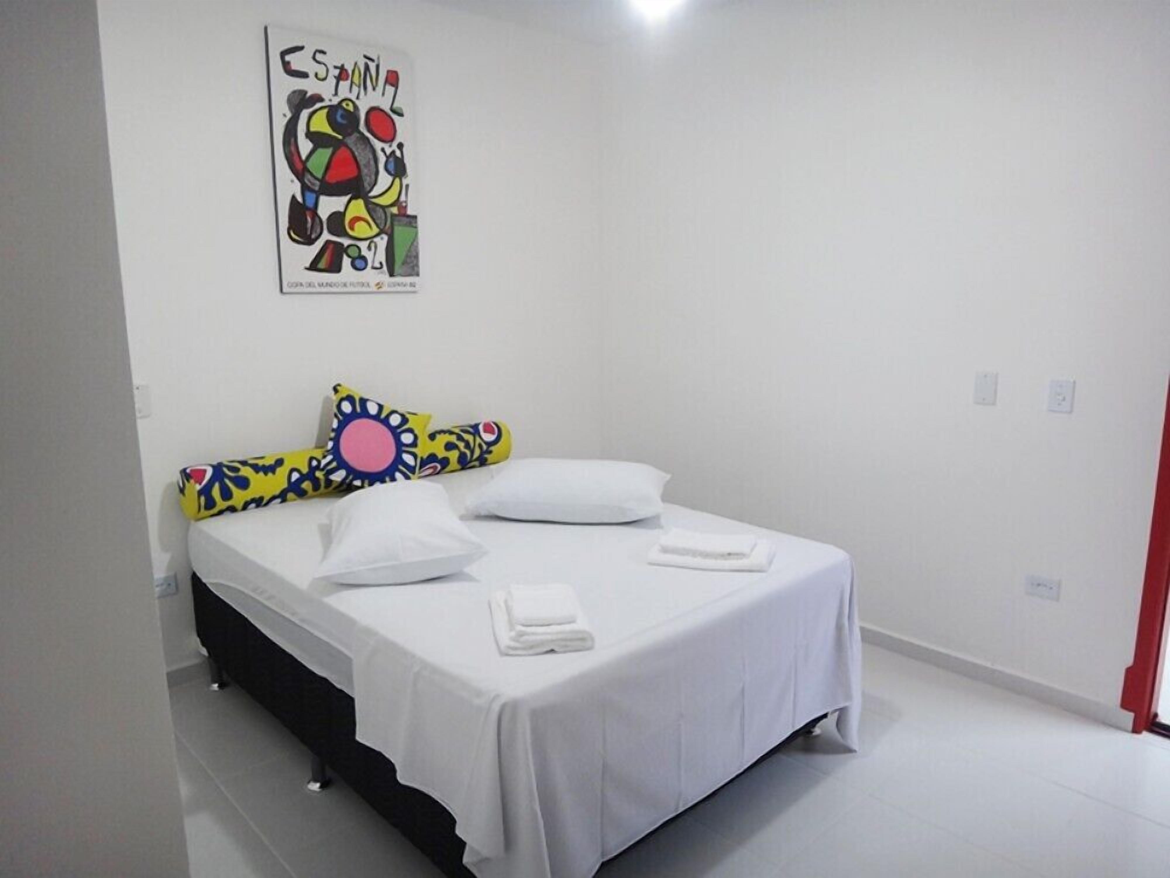 A bedroom with a bed, white bedding, colorful pillows, and a poster on the wall.