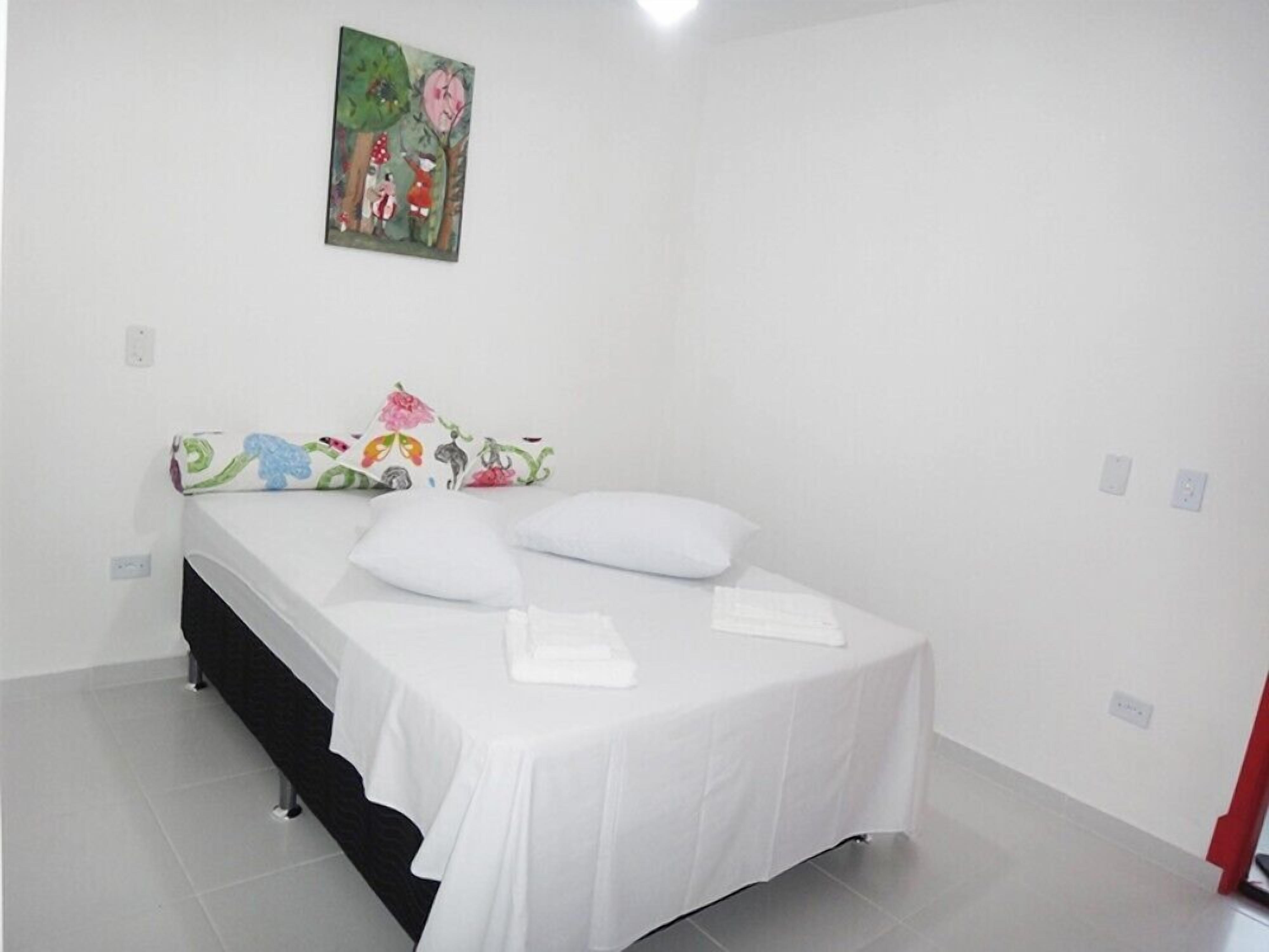 A clean, white bedroom with a bed, pillows, and a colorful headboard.