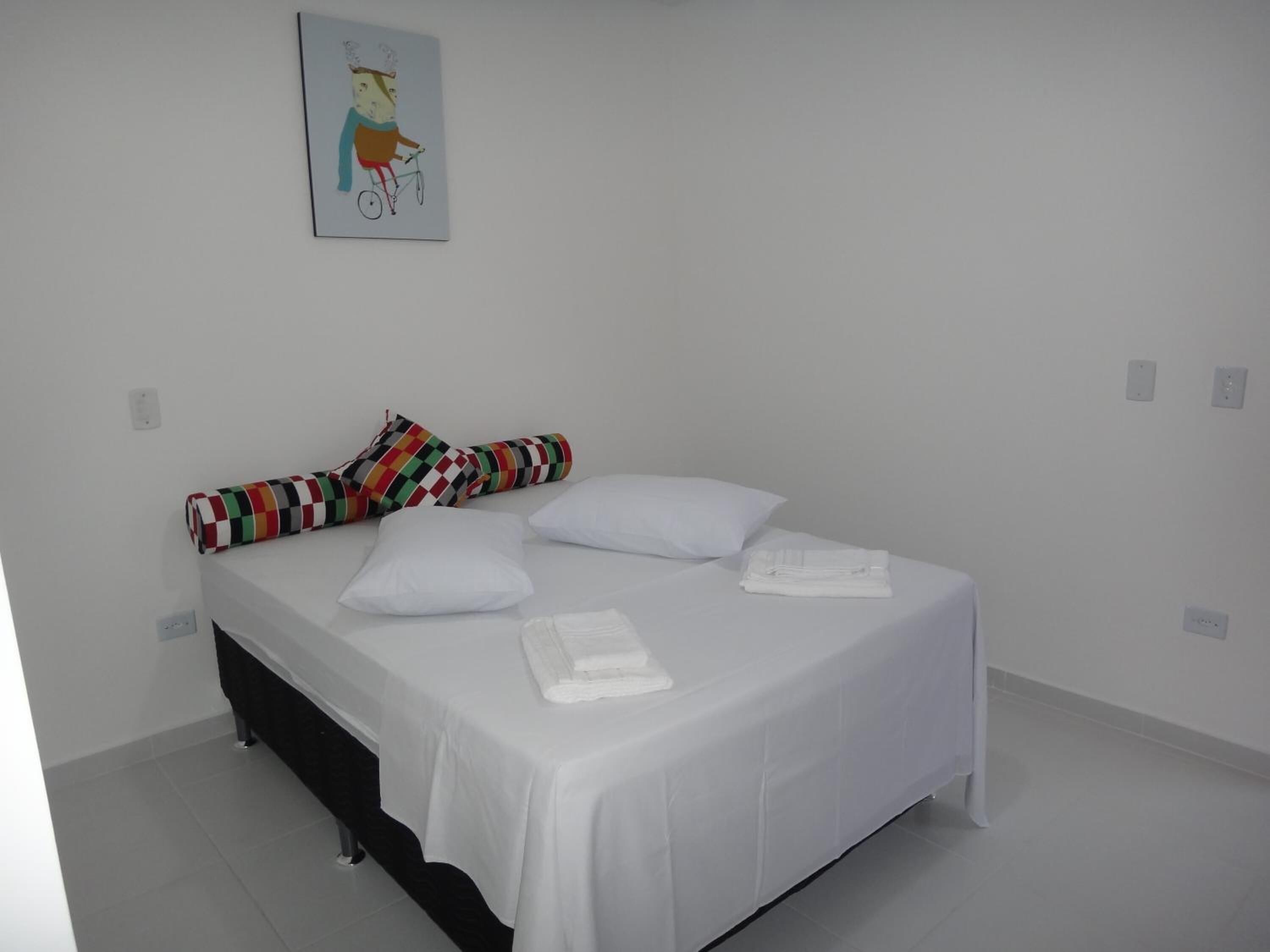 A single-bed room with a white bedspread, two pillows, a colorful striped pillow, and a folded white towel on the bed.