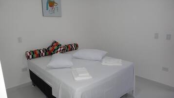 A single-bed room with a white bedspread, two pillows, a colorful striped pillow, and a folded white towel on the bed.