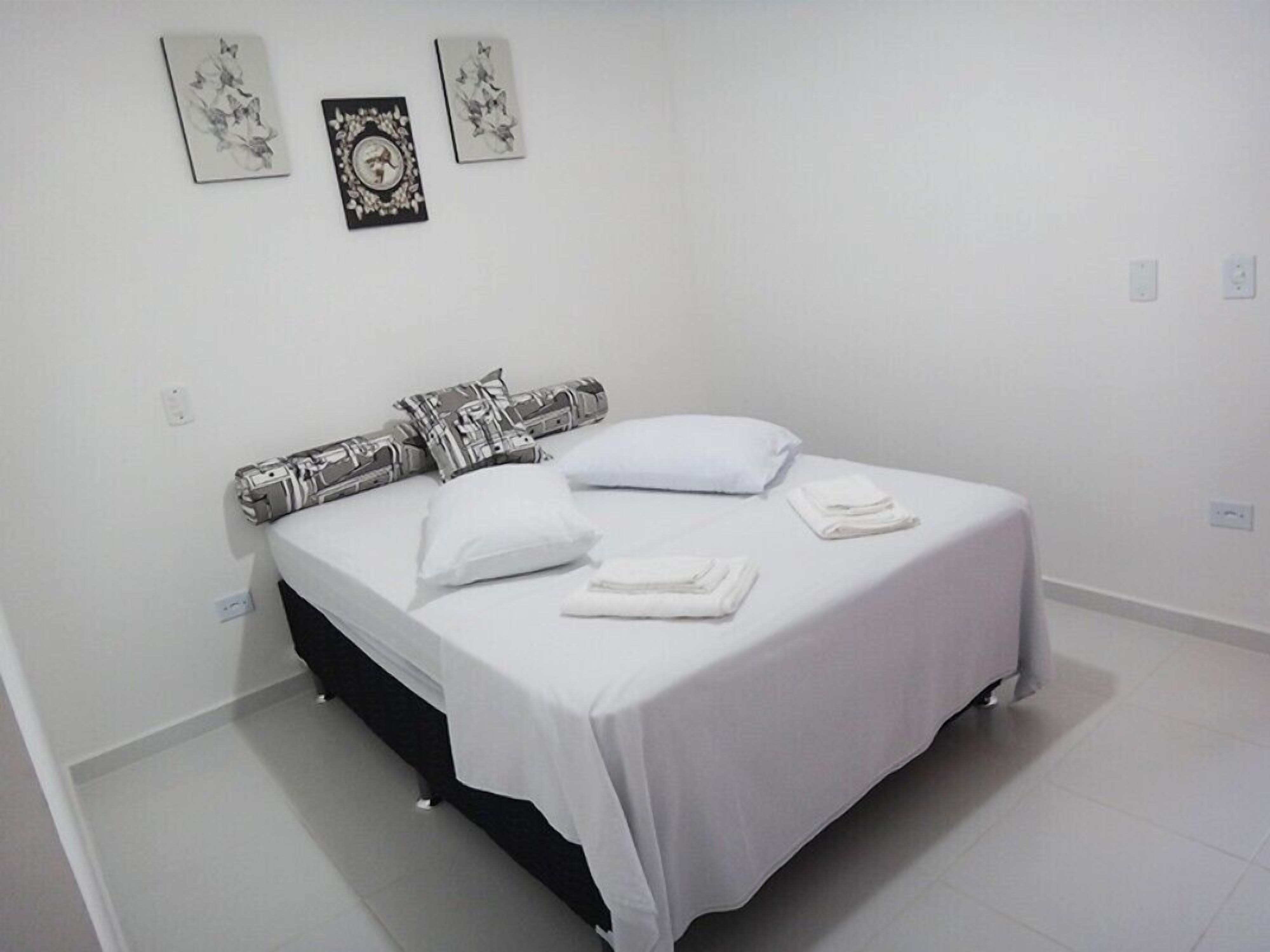 Una cama bien hecha con sábanas blancas y un cabecero negro, acompañada de dos almohadas y toallas dobladas.