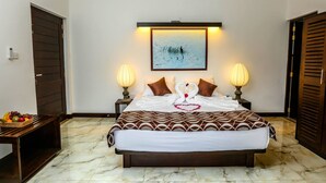 A neatly arranged hotel room with a large bed, two bedside lamps, a framed artwork above the bed, and a fruit basket on a small table beside the bed. - Huluganga Ridge (Teldeniya)