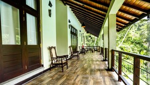 A covered veranda with wooden flooring and furniture, overlooking a lush green landscape. - Huluganga Ridge (Teldeniya)