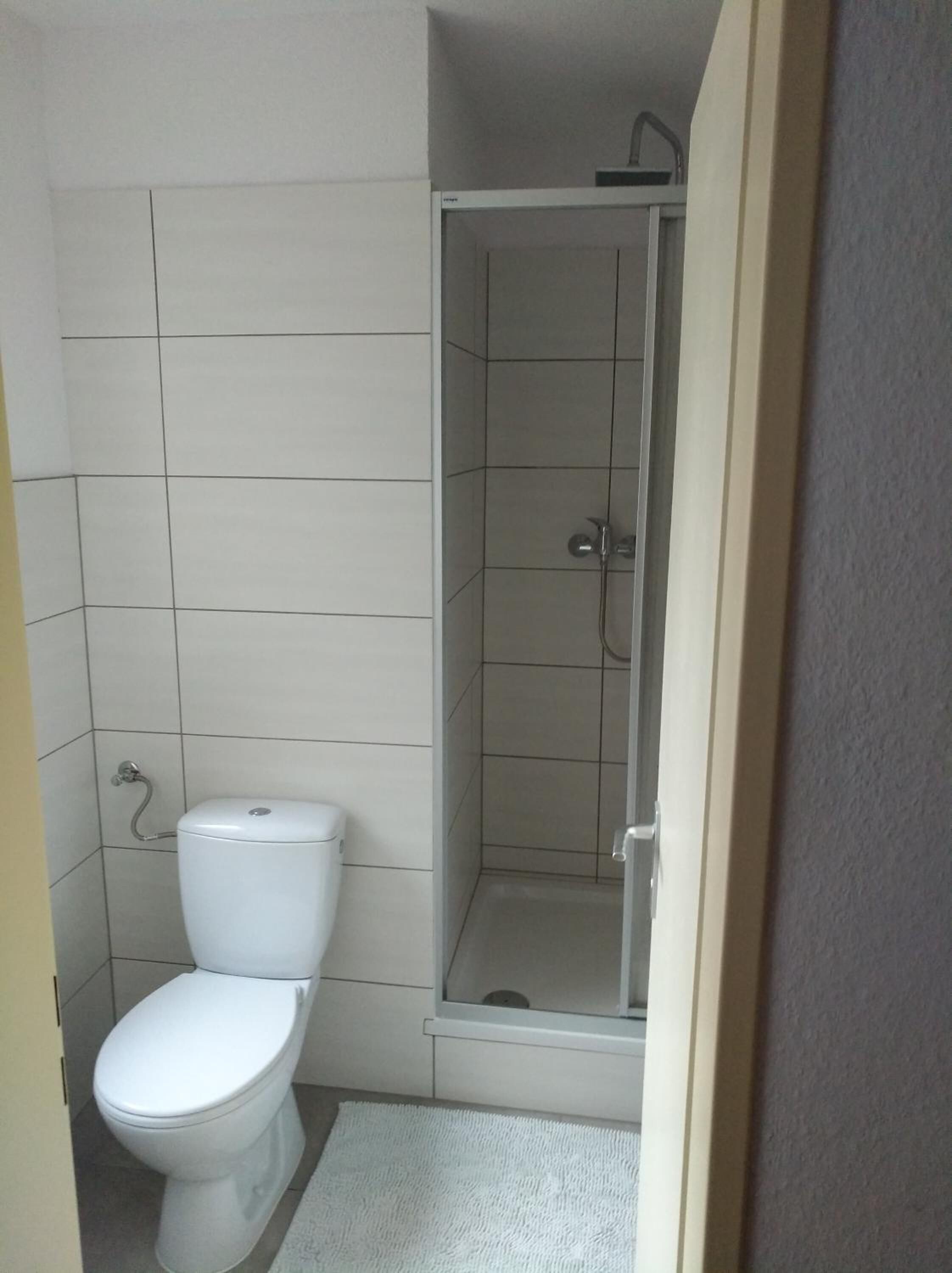 A small, clean bathroom with a toilet, a shower, and a tiled floor.