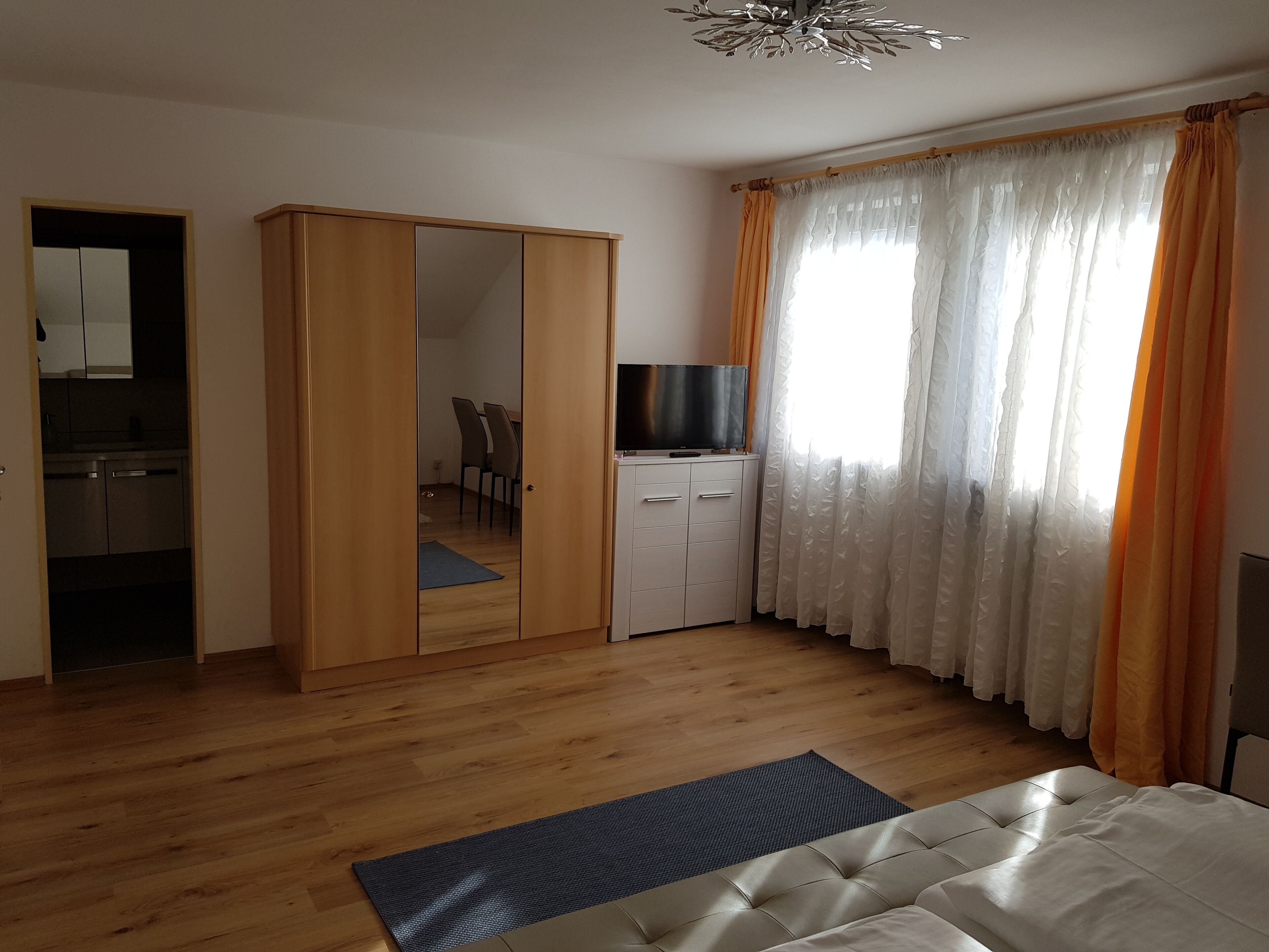 A bedroom with a wardrobe, a TV, a bed, and a window with curtains.