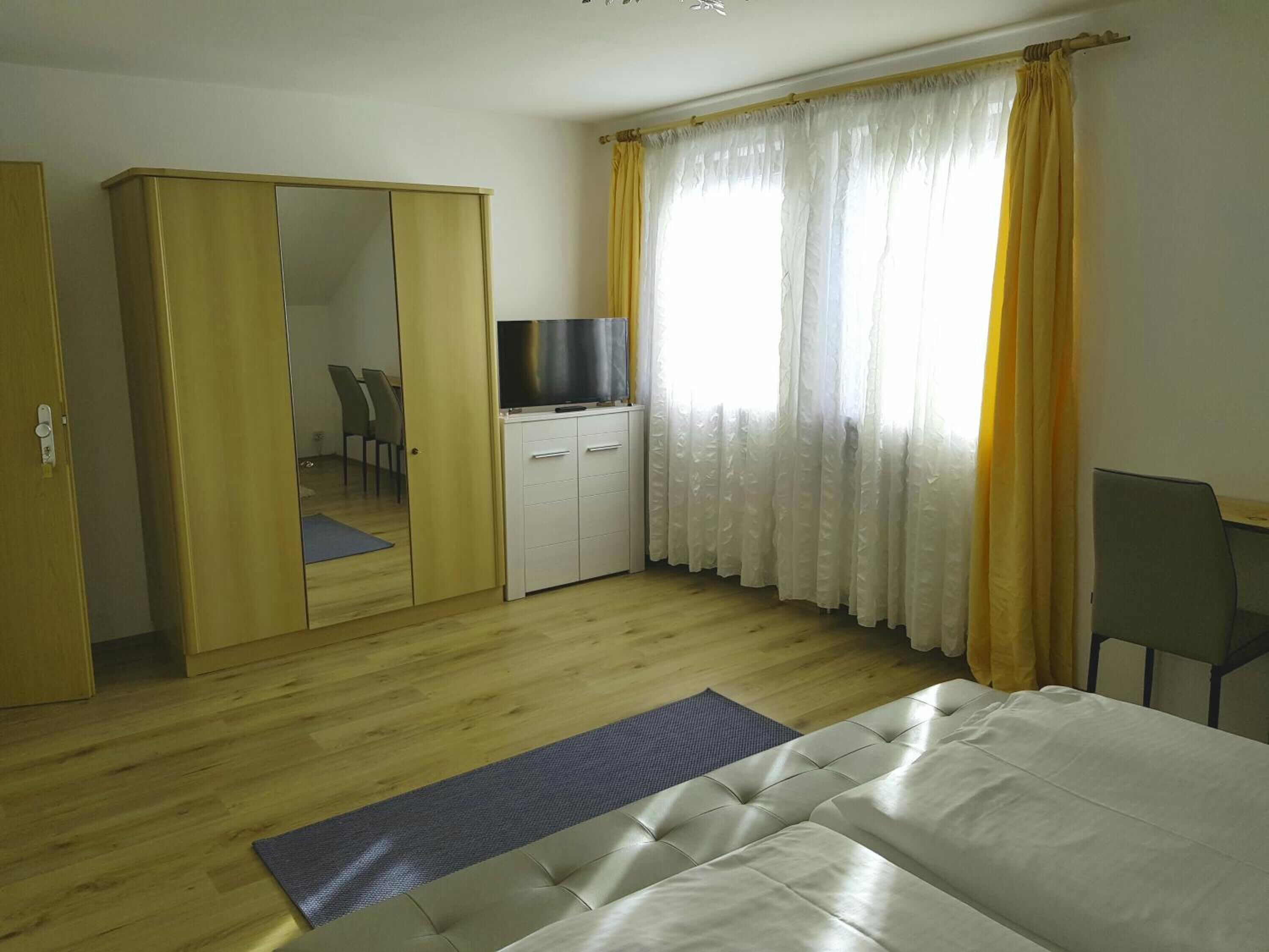 Un dormitorio con cama, armario, escritorio, silla y televisor.