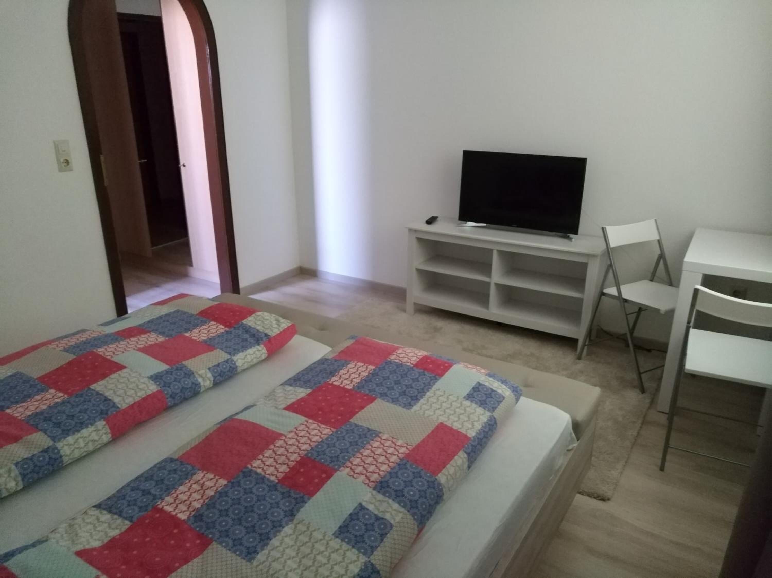 Ein Schlafzimmer mit zwei Betten, einem Fernseher auf einem Schrank, einem Schreibtisch und einem Stuhl.