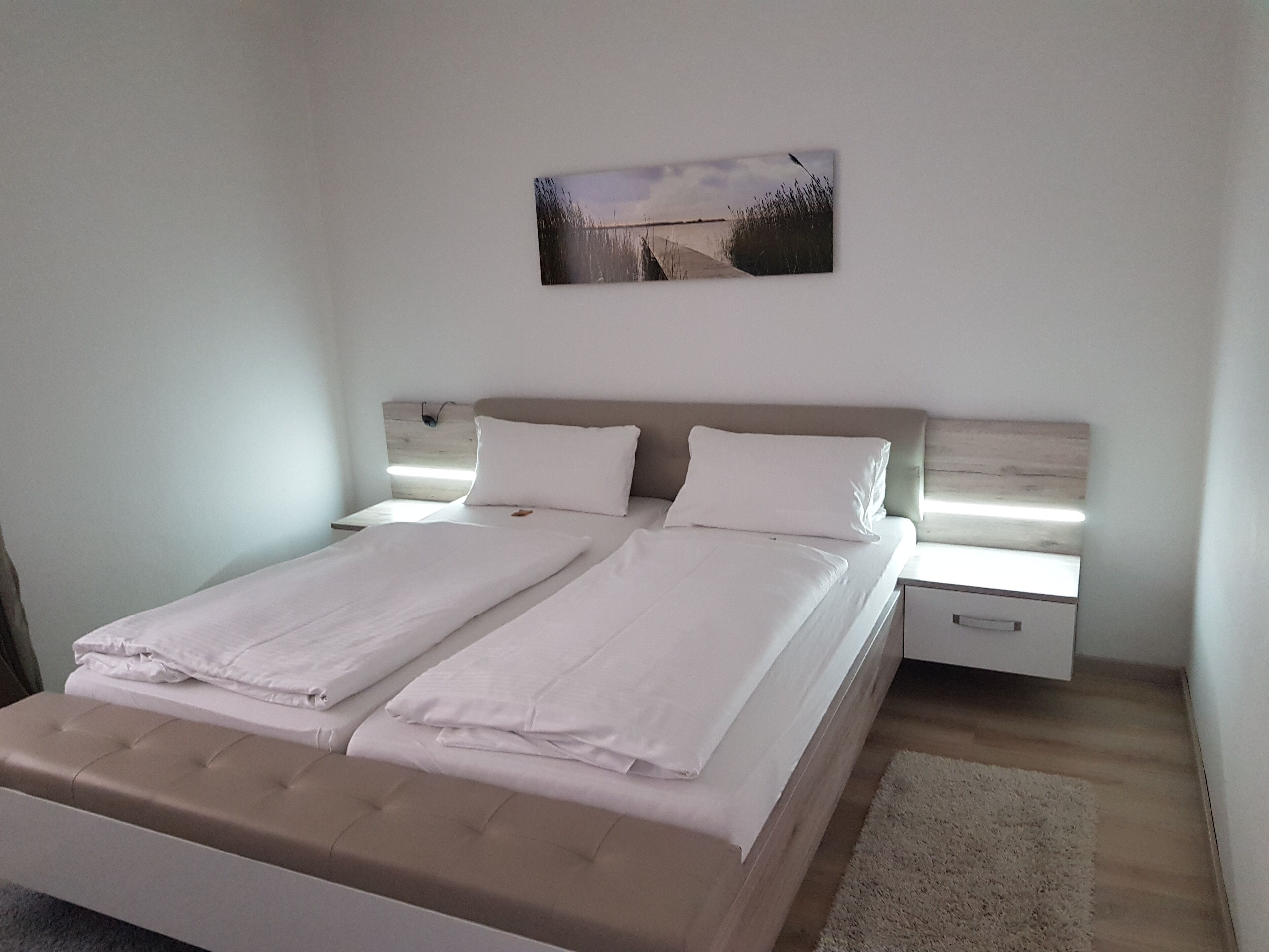 A double bed with a wooden headboard, two bedside tables, and a wall-mounted picture.