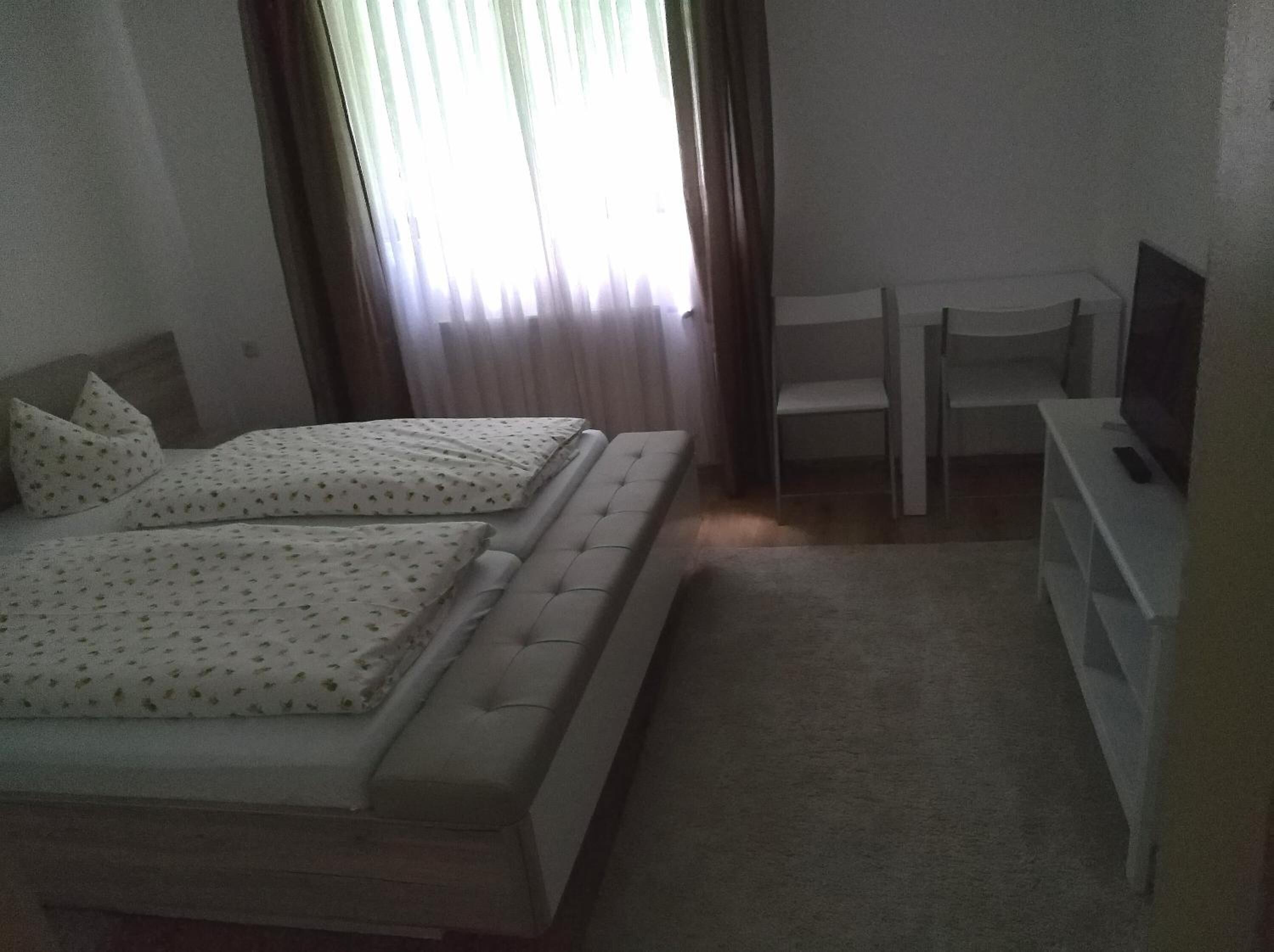 A bedroom with two beds, a TV, and a chair.