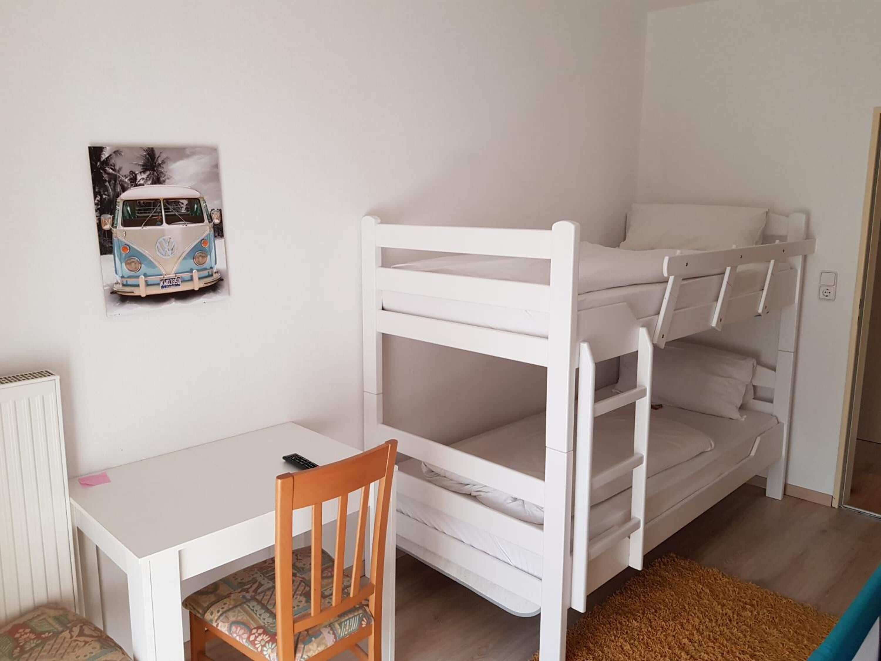 Un letto a castello con struttura bianca, una piccola scrivania con una sedia e un termosifone.