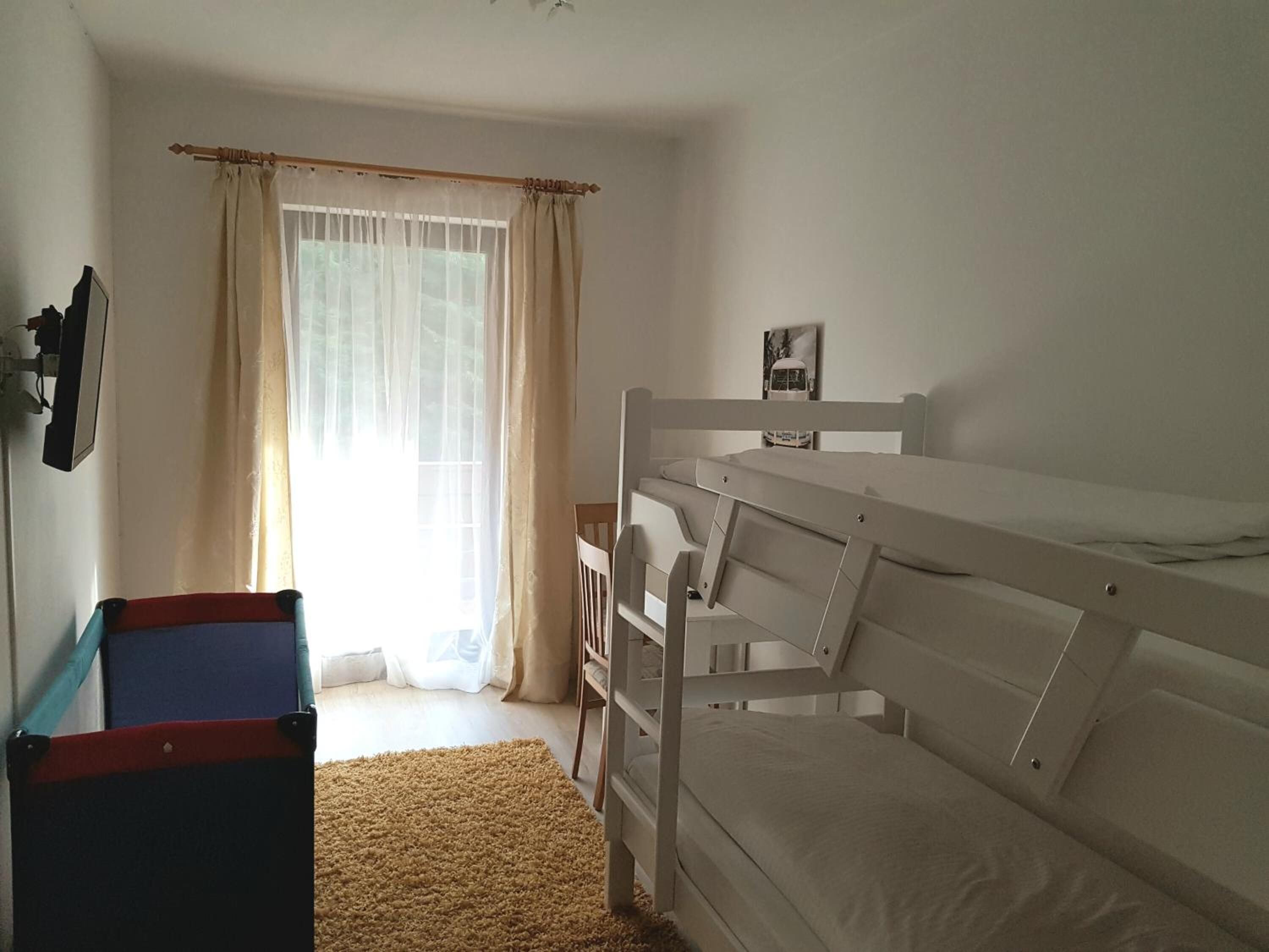 Habitación con literas, ventana, cortinas, una mesita y un cuadro en la pared.