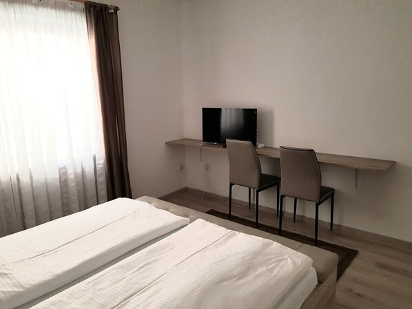 Habitación de hotel con cama, escritorio y dos sillas, televisión y ventana con cortinas.