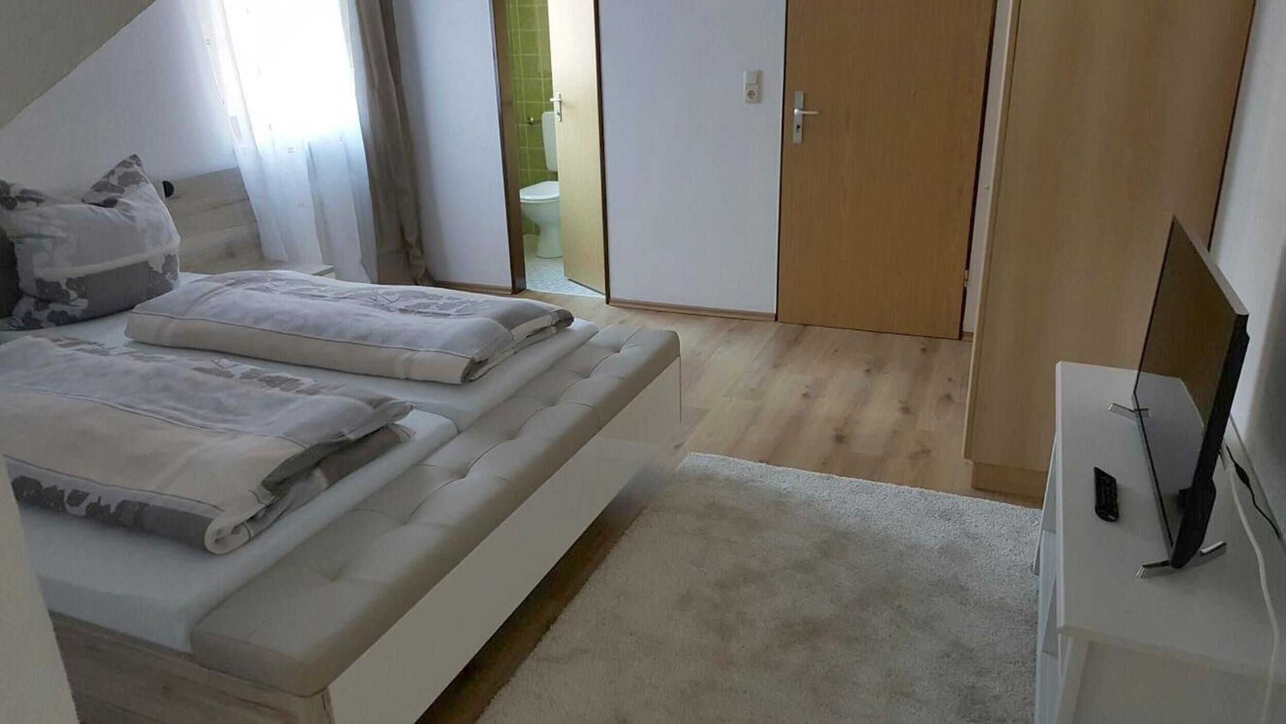 Una camera da letto con un letto, una TV su un mobile e una porta che dà su un bagno.