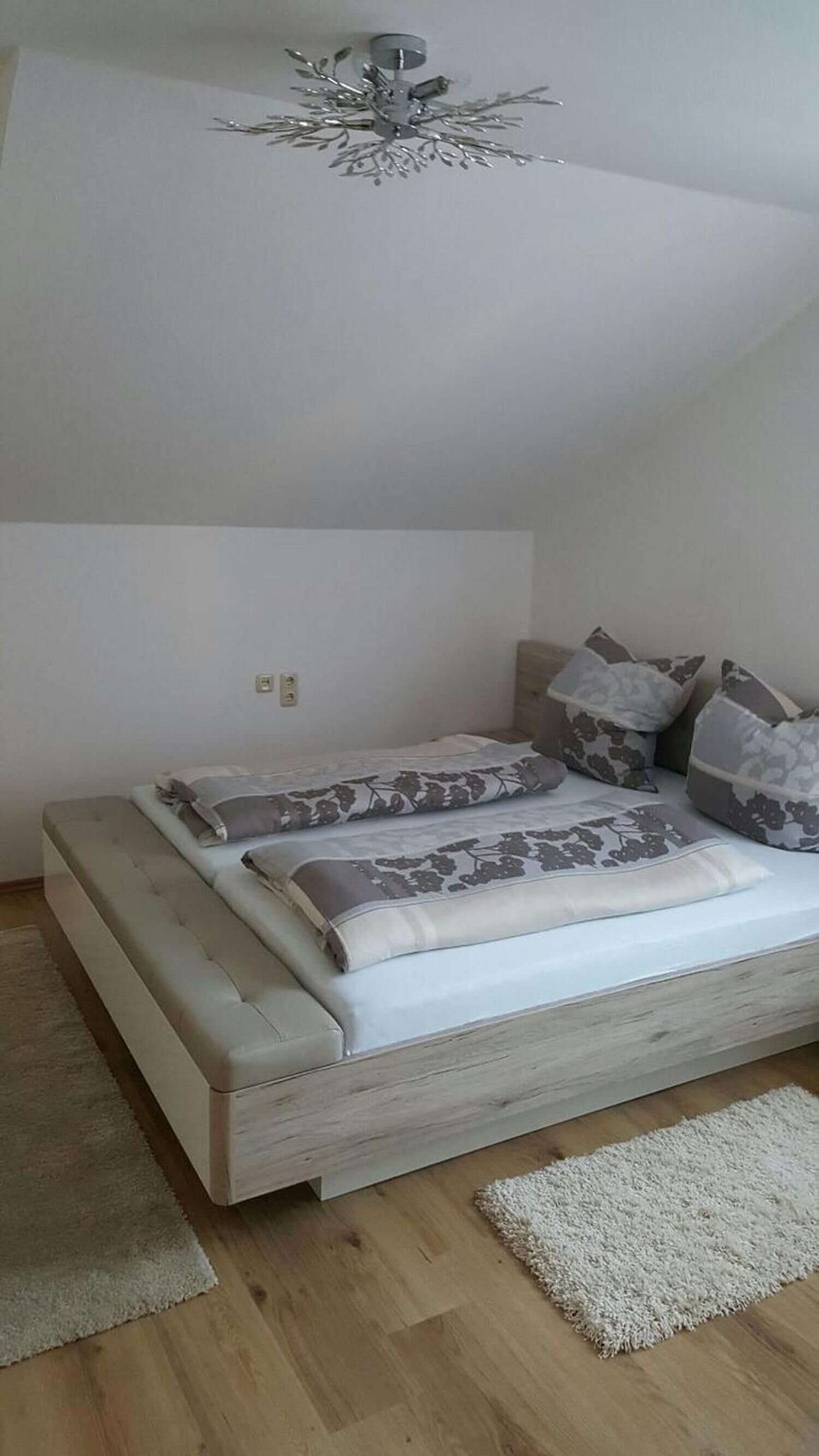 A bedroom with a bed, pillows, a ceiling fan, and a light switch on the wall.