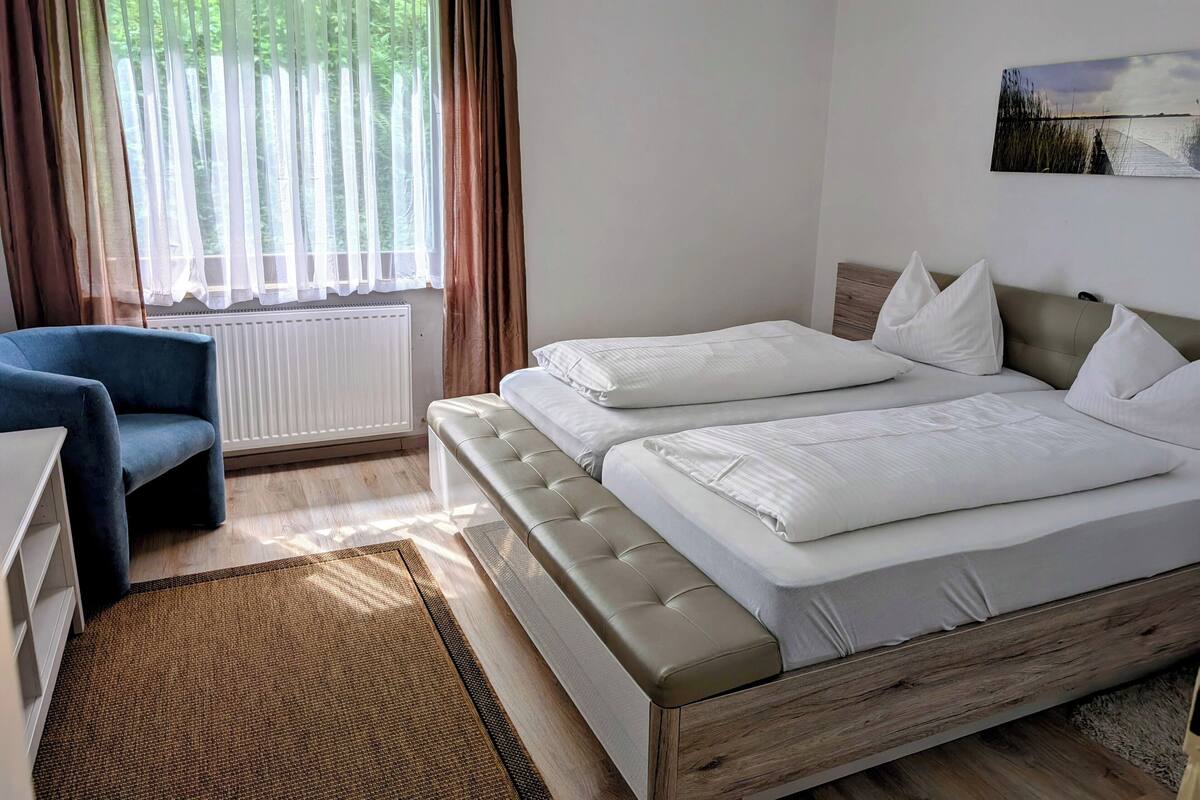 Une chambre à coucher avec un lit, une chaise, un radiateur et une fenêtre avec des rideaux.
