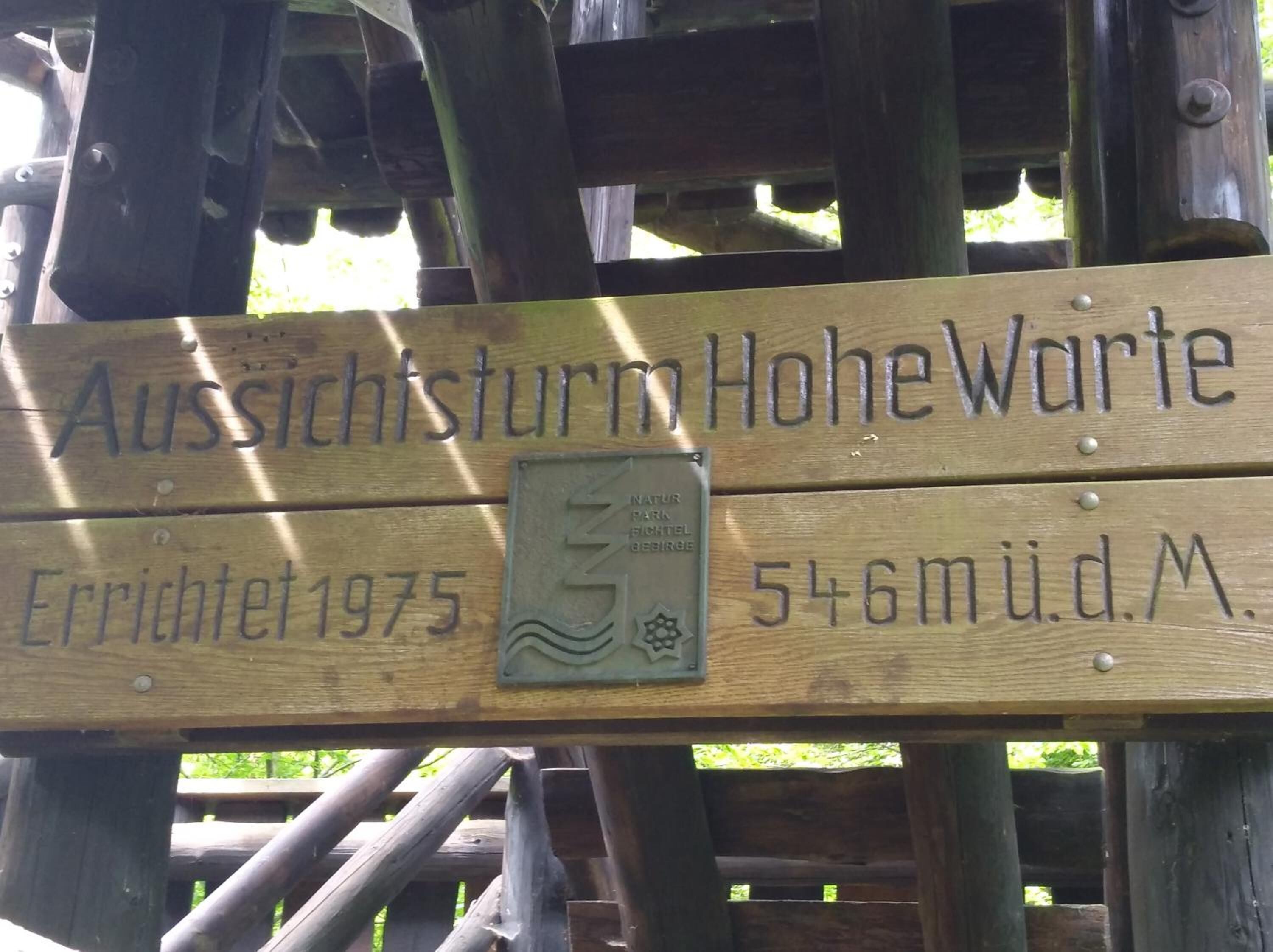 Un letrero de madera con el texto "Aussichtsturm Hohewarte" y "Construido en 1975".