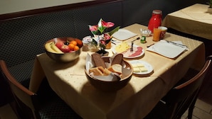Una mesa de comedor con diversos alimentos, incluyendo pan, queso y frutas, además de una tetera roja.