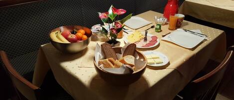 Una mesa de comedor con diversos alimentos, incluyendo pan, queso y frutas, además de una tetera roja.