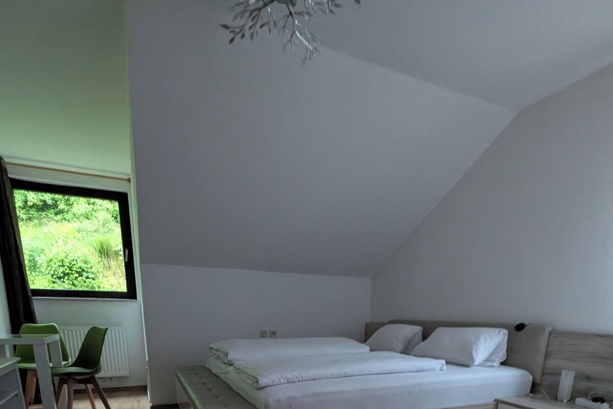 Une chambre moderne avec un grand lit, une table de chevet, une chaise et une vue sur la verdure.