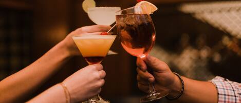 Two people holding cocktail glasses with a lime wedge and a cherry.