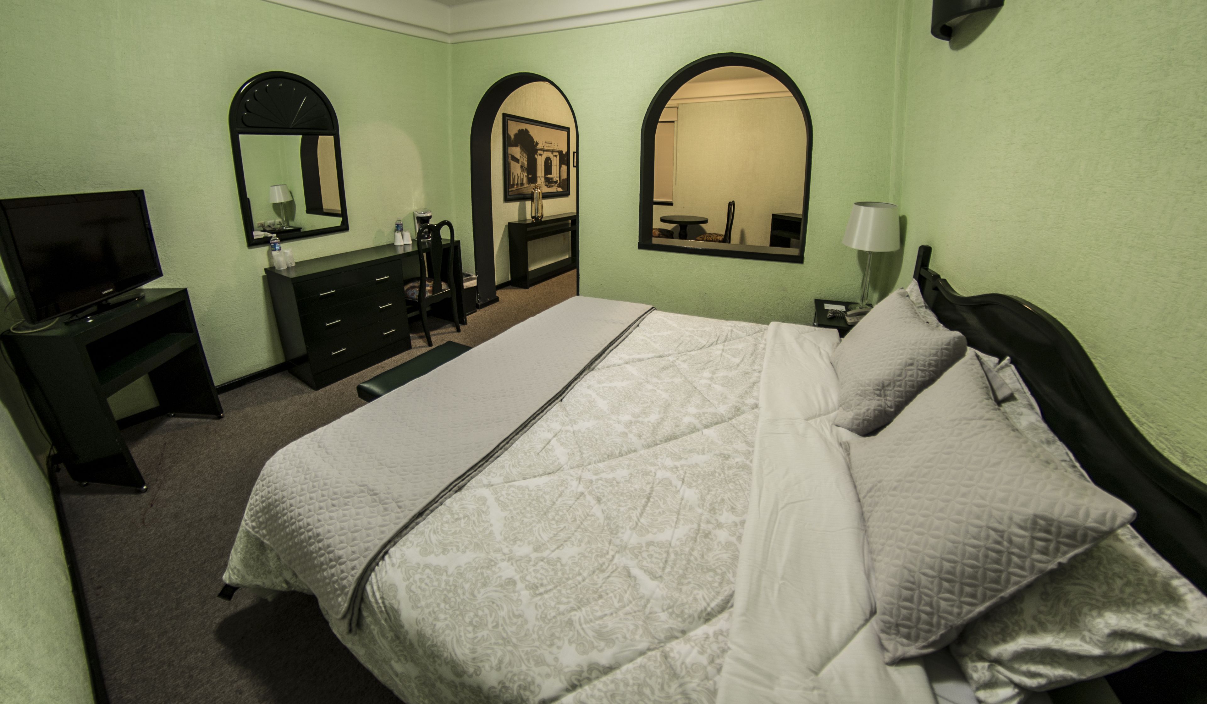 A hotel room with a bed, a TV, a dresser, and two arched mirrors.