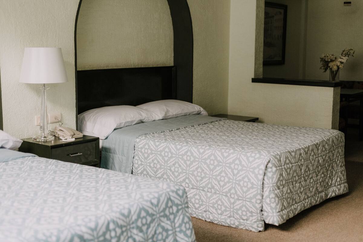 A hotel room with two beds, a nightstand with a lamp, and a mirror above the bed.