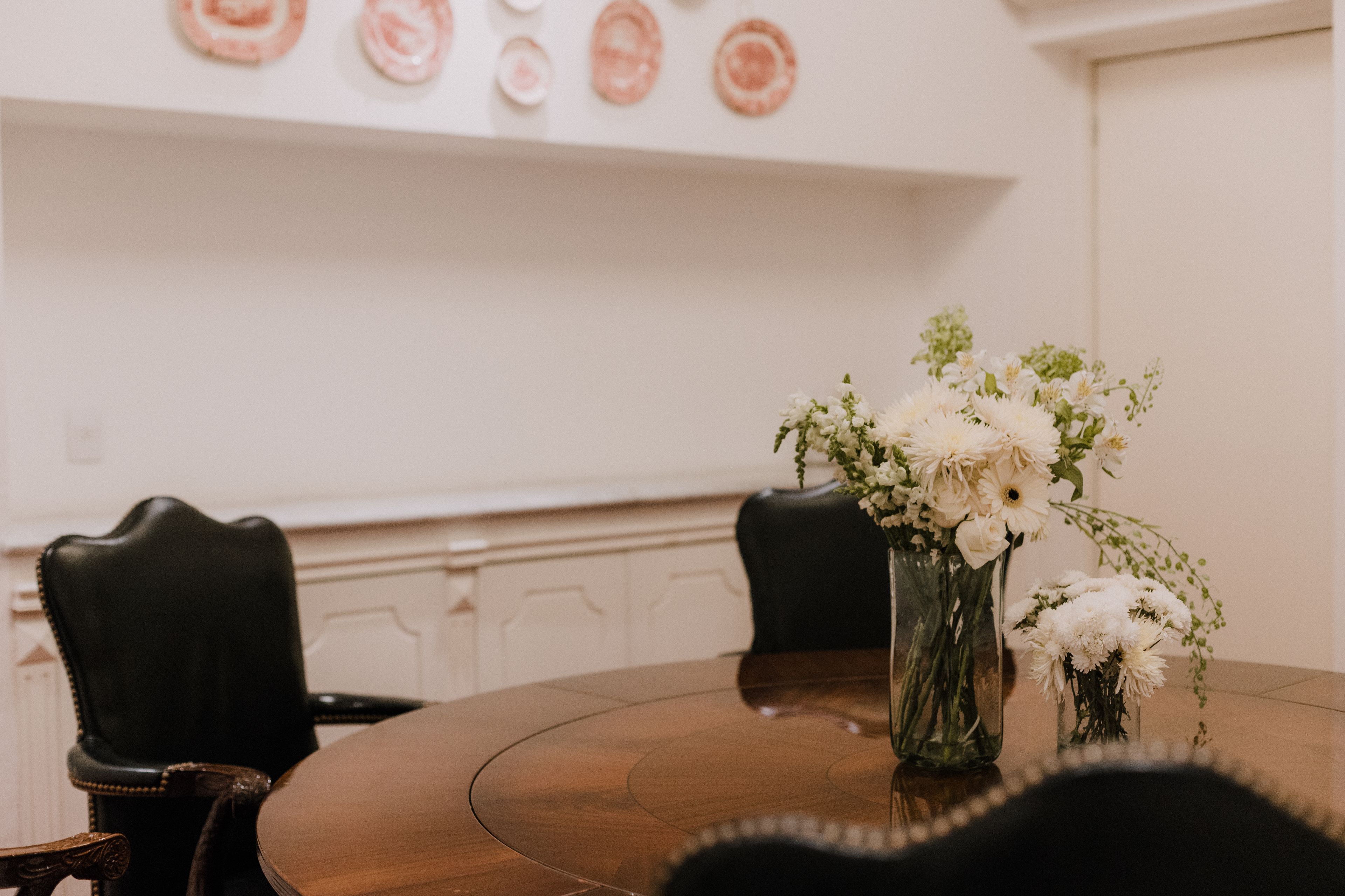 Ein Konferenztisch mit Stühlen, eine Vase mit Blumen und eine Wand mit dekorativen Tellern.